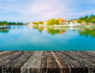 Ahşap iskele ya da gölün bulanık görüntüsü ve arka planda berrak gökyüzü olan eski ahşap bir masa.