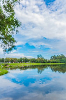 Göl kenarındaki insanların soyut bulanık görüntüsü ve arka plandaki mavi gökyüzü. (dikey)