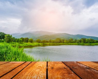 Eski ahşap bir masa ve arka planda yağmurlu gökyüzü ve dağlı bir göl.