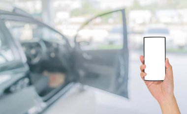Erkek eli modern bir dokunmatik ekranlı telefon tutuyor ve ticari arabaların görüntüsü araba dükkanının vitrininde duruyor..