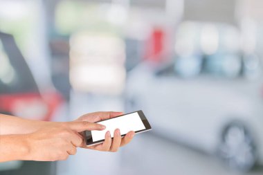 Erkek eli modern bir dokunmatik ekranlı telefon tutuyor ve ticari arabaların görüntüsü araba dükkanının vitrininde duruyor..