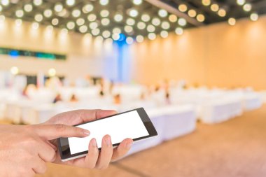 Erkek eli boş beyaz ekran akıllı telefonu tutuyor ve oditoryum odası arkaplanının bulanık görüntüsü .