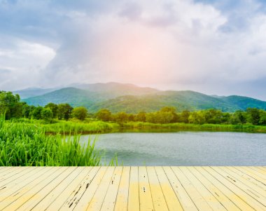 Eski ahşap bir masa ve arka planda yağmurlu gökyüzü ve dağlı bir göl.