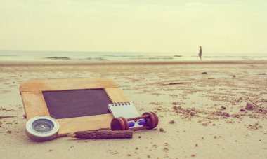 Arka planda bulanık deniz olan yaratıcı fikir için yazı tahtası ve kırtasiye malzemelerinin eski moda seyahat tonu görüntüsü. (karatahtaya seçici odaklanma)