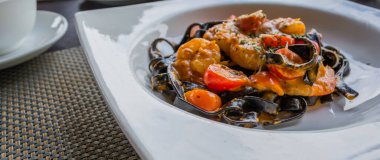 Beyaz tabakta karidesli mürekkep balığı mürekkebi makarnası resmi.