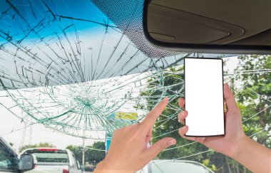 Beyaz ekranlı akıllı telefon ve kırık araba ön camlı erkek eli görüntüsü araba kazasında içeriden fotoğraf çekiliyor..