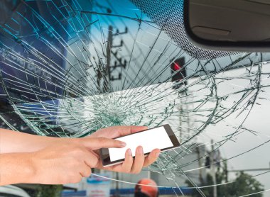 Beyaz ekranlı akıllı telefon ve kırık araba ön camlı erkek eli görüntüsü araba kazasında içeriden fotoğraf çekiliyor..