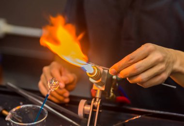 Cam üfleme makinesindeki cam alevlerin üzerindeki cam çubukla el ele tutuşma görüntüsünü kapat..