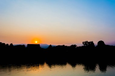 Arkaplanda ağaç ve günbatımı görüntüsü.