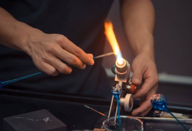 Cam üfleyici fabrikasındaki cam alevlerin üzerindeki el yapımı cam çubuğu yakın çekim görüntüsü. (ele odaklan)