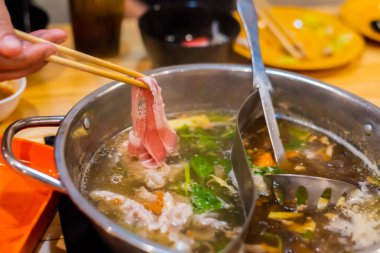 Kore Shabu restoranındaki sıcak kasenin üzerinde dilimlenmiş domuz eti resmi..