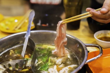 Kore Shabu restoranındaki sıcak kasenin üzerinde dilimlenmiş domuz eti resmi..