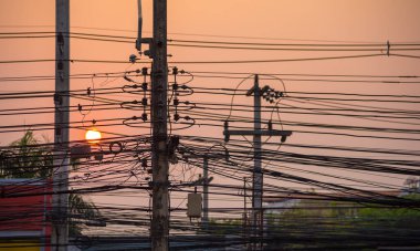 silhouette shot image of high voltage electric wire in city with sun on sunset sky in background.(focus on wire)