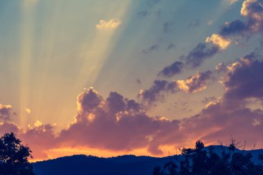 vintage tone image of sun crepuscular ray(beam) on the sky on day time with mountain for background usage.