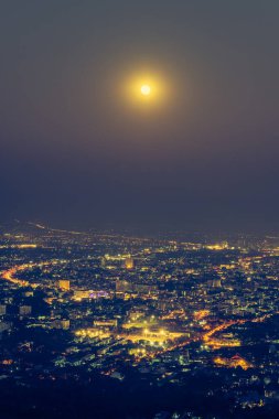 vintage tone long exposure shot vertical image of Chiang Mai province,Thailand the old city  view from high angle spot night time with super full moon.