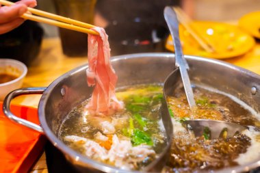 Kore Shabu restoranındaki sıcak kasenin üzerinde dilimlenmiş domuz eti resmi..