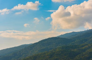 Tropikal yeşil dağ ormanının ve bulutlu gökyüzünün gündüz görüntüsü.