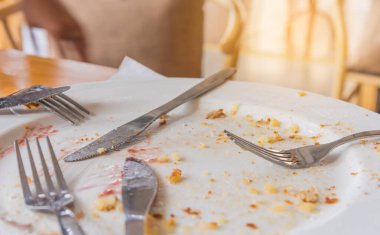 Masada çatal ve bıçakla beyaz tabakta kalan küçük bir parça pasta..