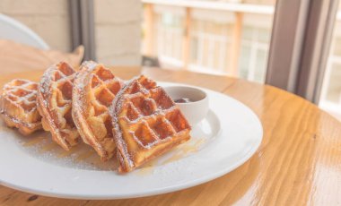 Pencerenin yanındaki tahta masada waffle yığını var.