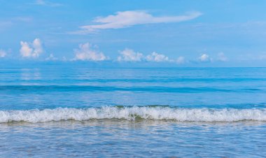 Arka planda mavi gökyüzü olan deniz kıyısındaki dalgaların görüntüsü.