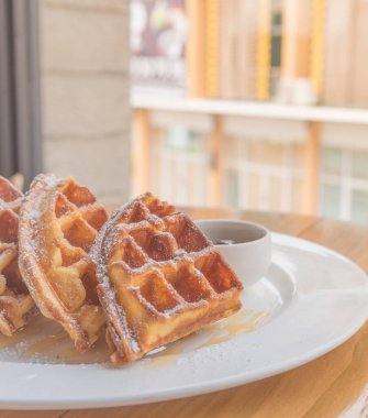 Tahta masanın yanındaki pencerenin yanında waffle yığını var..