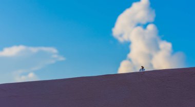 Arka planda gündüz vakti bulanık gökyüzü olan bisiklet sürücüsünün minyatür bebek fikri.