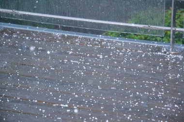 Dolu ve yağmur suyunun küçük beyaz taneleri kahverengi fayanslı balkonu kaplıyor. Kapalı çekim yağmur damlaları ve yağan bahar fırtınası sırasında ıslak zemine düşen buz gibi yumuşak dolu.. 