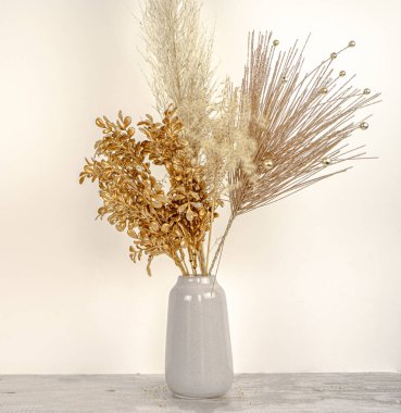 Beyaz bir duvar ve ahşap masa arkaplanındaki vazoda, yeni yıl altın dallı otların kompozisyonu. Tatil dekorasyonu konsepti. Kaliteli fotoğraf