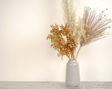 Beyaz bir duvar ve ahşap masa arkaplanındaki vazoda, yeni yıl altın dallı otların kompozisyonu. Tatil dekorasyonu konsepti. Kaliteli fotoğraf