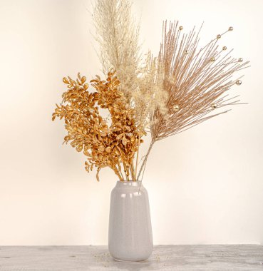  Beyaz bir duvar ve ahşap masa arkaplanındaki vazoda, yeni yıl altın dallı otların kompozisyonu. Tatil dekorasyonu kavramı