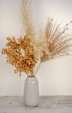 Beyaz bir duvar ve ahşap masa arkaplanındaki vazoda, yeni yıl altın dallı otların kompozisyonu. Tatil dekorasyonu konsepti. Kaliteli fotoğraf