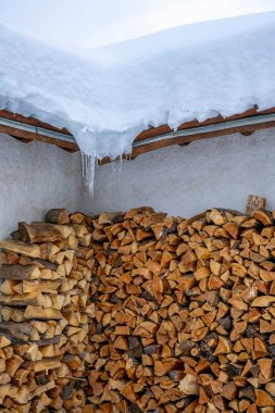 Kışın karlı bir evin duvarında bir sürü kuru odun yığını.