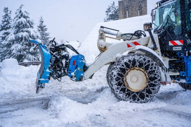 Auron, Fransa 01.01.2021 Traktör Fransız Alpleri 'ndeki kayak merkezinin yanındaki yoldaki büyük kar yığınlarından karı kaldırıyor.