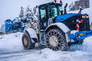 Auron, Fransa 01.01.2021 Traktör Fransız Alpleri 'ndeki kayak merkezinin yanındaki yoldaki büyük kar yığınlarından kar temizliyor. Yüksek kalite fotoğraf