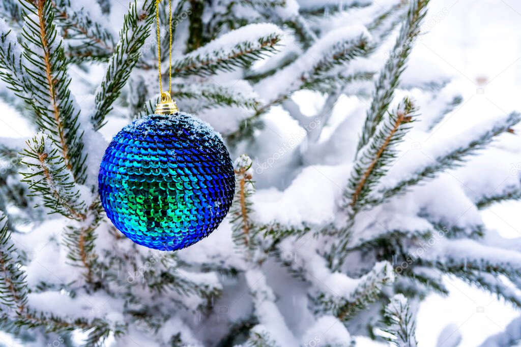 Tidewater green Christmas ball hangs on a snow-covered branch of a Christmas tree. Blue light bokeh background. New Year, greeting and holiday card, banner. High quality photo