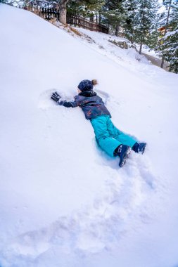 Renkli kışlık takım elbiseli komik çocuk kar tepesine tırmanıyor. Çocuklar karlı ormanda oynayıp zıplıyorlar. Kışın karla oynayan çocuk. 