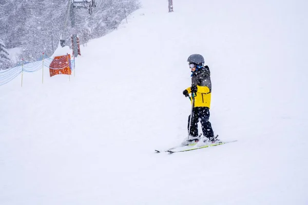 Garoto esquiando na encosta, fazer uma lição de esqui durante uma queda de neve, neve fresca na floresta durante uma queda de neve. Jovem esquiador esquiando com máscara de esqui e capacete na estação de esqui Auron em francês Apls. — Fotografia de Stock