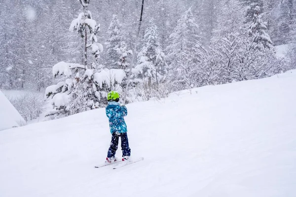 Dívka, která zvedá lano na vleku v modrém sportovním oblečení na horách lyžařského střediska, se během sněžení učí lyžovat. Auron ski resort ve francouzských Apls. — Stock fotografie