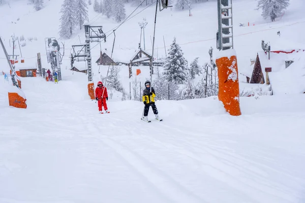 AURON, FRANÇA - 01.01.2021: Instrutor profissional de esqui e levantamento de crianças na corda de elevação de arrasto de esqui até a montanha durante a queda de neve. Conceito de férias ativas de família e crianças. — Fotografia de Stock