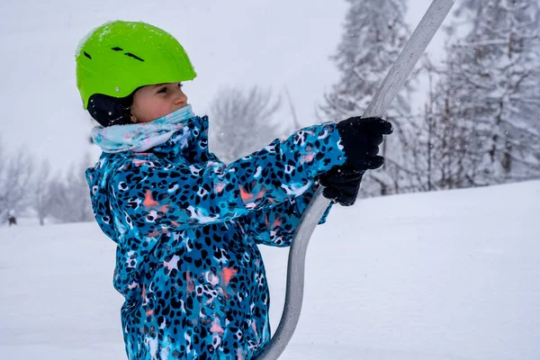 Sfondo sfocato. Una ragazza che si solleva sulla fune da skilift in costume sportivo blu sulla montagna della stazione sciistica fa una lezione di sci durante una nevicata. Comprensorio sciistico in montagna francese. — Foto Stock