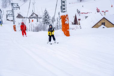 AURON, FRANCE - 01.01.2021: Profesyonel kayak hocası ve çocuk kar yağışı sırasında kayak kaldırma halatıyla dağa çıkıyor. Aile ve çocuklar aktif tatil kavramı. 
