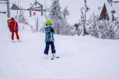 AURON, FRANCE - 01.01.2021: Profesyonel kayak hocası ve çocuk kar yağışı sırasında kayak kaldırma halatıyla dağa çıkıyor. Aile ve çocuklar aktif tatil kavramı. 