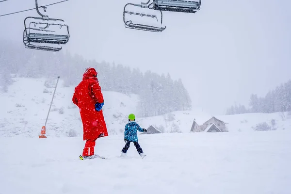 Επαγγελματίας δάσκαλος σκι μαθαίνει σε ένα παιδί να κάνει σκι σε μια πλαγιά βουνού. Μέρα που χιονίζει. Θολή εστίαση φόντου. Οικογενειακές και παιδικές διακοπές. — Φωτογραφία Αρχείου