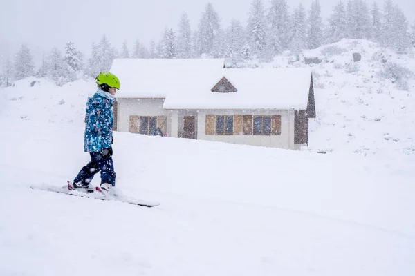 Downhill σκι κατά τη διάρκεια μιας βαριάς χιονόπτωση. Παιδικό σκι στα βουνά. Ενεργό παιδί με κράνος και γυαλιά. Αγώνας σκι για μικρά παιδιά. Μαθήματα σκι για παιδιά σε αλπική σχολή. Θολή εστίαση φόντου — Φωτογραφία Αρχείου