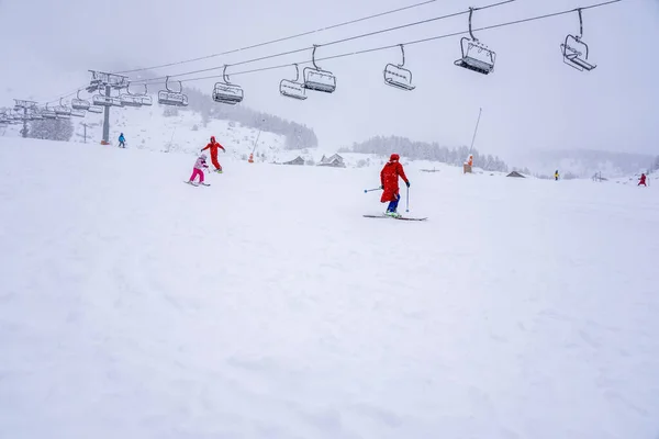 Downhill σκι κατά τη διάρκεια μιας βαριάς χιονόπτωση. Επαγγελματίες εκπαιδευτές σκι και παιδιά σε μια πλαγιά θέρετρο στα βουνά. Αγώνας σκι για μικρά παιδιά. Θολή εστίαση φόντου — Φωτογραφία Αρχείου