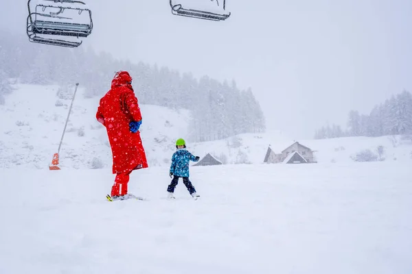 Professional ski instructor is teaching a child to ski on a mountain slope. Snowfall day. Blurred focus background. Family and children vacation. — Stock Photo, Image