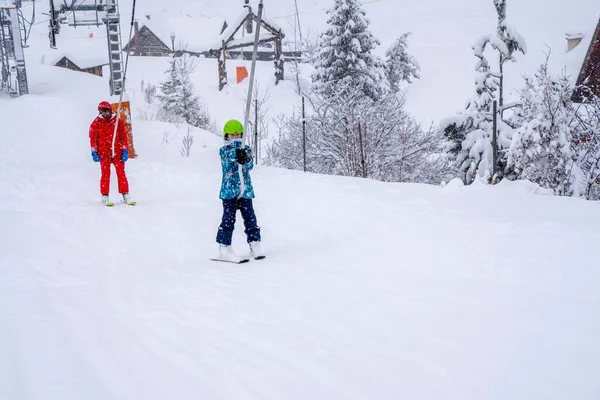 AURON, FRANCE - 01.01.2021: Επαγγελματίας εκπαιδευτής σκι και ανύψωση παιδιών στο σχοινί του τελεφερίκ σκι προς το βουνό κατά την χιονόπτωση. Οικογένεια και παιδιά έννοια ενεργό διακοπές. — Φωτογραφία Αρχείου