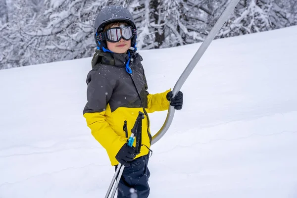 Un garçon soulevant sur la corde de téléski en tenue sportive lumineuse sur la montagne de la station de ski faire une leçon de ski lors d'une chute de neige. Station de ski en montagne française. Fond de foyer doux. — Photo