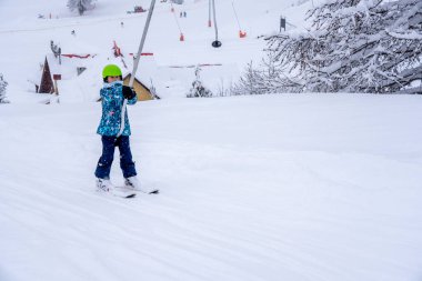 Bulanık odak arkaplanı. Kayak merkezindeki dağda mavi spor kıyafetiyle kayak kaldıran bir kız kar yağışı sırasında kayak dersi verir. Fransız dağında kayak merkezi. Yüksek kalite fotoğraf
