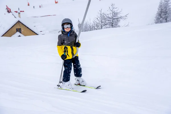 Bulanık odak arkaplanı. Kayak merkezindeki dağda parlak spor kıyafetleriyle kayak kaldıran bir çocuk kar yağışı sırasında kayak dersi veriyor. Fransız dağlarında kayak merkezi.. — Stok fotoğraf